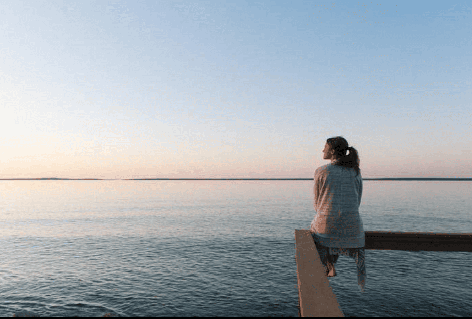 Mujer sentada en calma observando el horizonte mientras reflexiona sobre el cansancio emocional, la saturación energética y la importancia del autocuidado consciente. pedir ayuda
